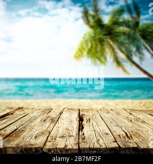 Tischhintergrund mit Platz für Ihre Dekoration. Verschwommener Strandhintergrund mit grünen Kokospalmen. Sonniger Tag mit blauem Himmel und Sonnenlicht. Sommerzeit. Stockfoto