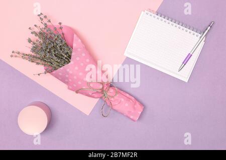 Blumenstrauß aus Lavendel, Kosmetikbecher und leeres Notizbuch öffnen. Frauen Lifestyle Minimalkonzept Stockfoto