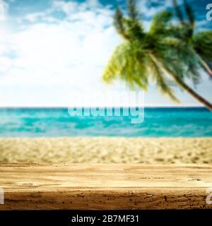 Tischhintergrund mit Platz für Ihre Dekoration. Verschwommener Strandhintergrund mit grünen Kokospalmen. Sonniger Tag mit blauem Himmel und Sonnenlicht. Sommerzeit. Stockfoto