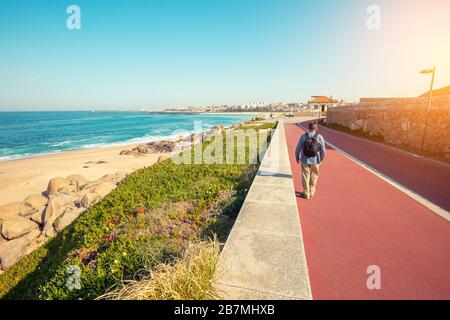 Promenade entlang des Meeres und des Atlantiks im Frühling. Ein Mensch geht auf die Böschung. Schöne Bucht an einem sonnigen Tag. Blick auf die Stadt Porto am Horizont Stockfoto