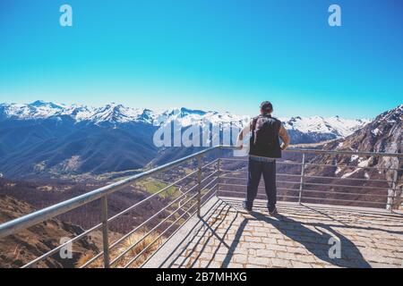 Ein Tourist steht auf einem Aussichtspunkt über dem Tal gegen schneebedeckte Berge. Ein Mann blickt auf das schöne Panorama der Berge. National Stockfoto