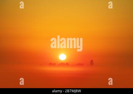 Ländliche Landschaft. Magischer oranger Sonnenaufgang auf dem Feld an einem frühen nebligen Morgen. Minimalistische Landschaft Stockfoto