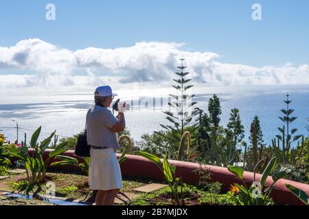 Reifere Frauen, die den Blick über Funchal Madeira, Portugal, auf einer Levada und mit Berg und einem bewölkten Himmel im Hintergrund betrachten. Stockfoto