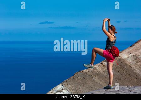 Frau, die Yoga praktiziert und auf den Felsen von Vulcano Island, Äolischen Inseln, Italien springt. Mittelmeer im Hintergrund. Stockfoto