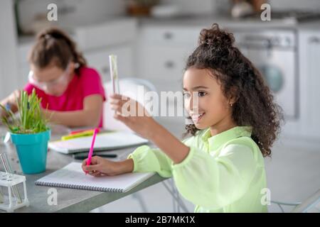 Liebliches lockiges Mädchen mit Reagenzglas und Marker. Stockfoto