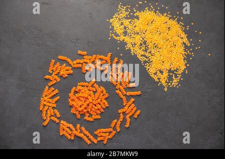 Orangefarbene Teigspiralen und Linsen vor dunklem Hintergrund. Diät- und Lebensmittelkonzept Stockfoto