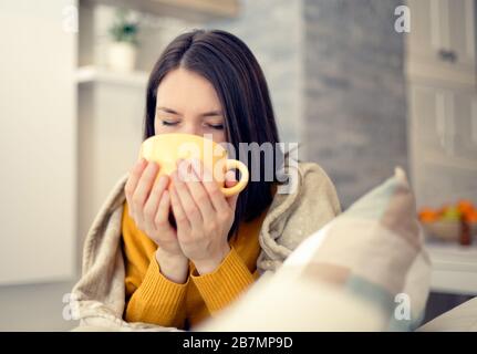 Kranke junge Frau mit Grippevirus zu Hause, die Tee mit Decke trinkt Stockfoto