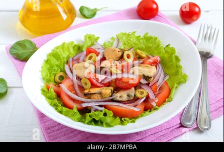 Salat aus marinierten Muscheln, frischen Tomaten, roten Zwiebeln, Oliven in einer Schüssel auf weißem Holzhintergrund Stockfoto