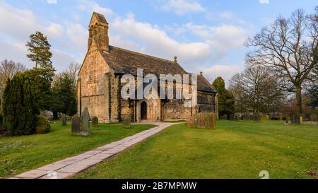 Außenansicht der historischen Kirche St. Johannes der Täufer, Kirchenhof-Gedenkstätten und Pfad, der zu einem geschnitzten normannischen Türbogen führt - Adel, Yorkshire, England Großbritannien Stockfoto