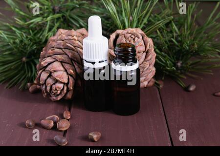 Zedernöl in einer Glasflasche und Zedernkegel mit Nüssen auf einem alten Holztisch. Stockfoto