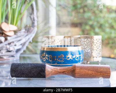 Haulerwijk - 07. märz 2020: Haulerwijk, Niederlande. Blaue und goldene indische Gesangsschale aus sieben Metallen mit einem Holzstreifer auf einem Glas Stockfoto