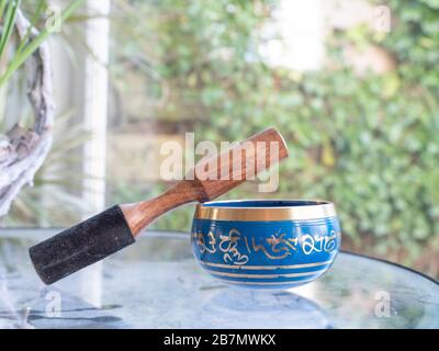 Haulerwijk - 07. märz 2020: Haulerwijk, Niederlande. Blaue und goldene indische Gesangsschale aus sieben Metallen mit einem Holzstreifer auf einem Glas Stockfoto
