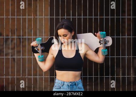 Junge Frau sitzt auf Ihrem skate in einem alten industriellen Straße lehnte sich gegen Metall Zaun Stockfoto