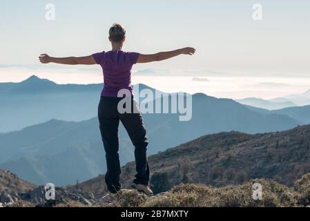 Wanderfrau mit offenen Armen im Kreuz auf dem Berg. Stockfoto