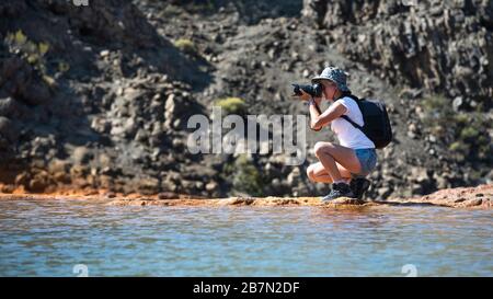 Ein Fotograf mit DSLR-Kamera, der am Fluss und in den Bergen spaziert. Stockfoto