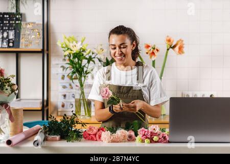 Lächelnde Frau, die Blumen am Tisch hält und einen Blumenstrauß arrangiert Stockfoto
