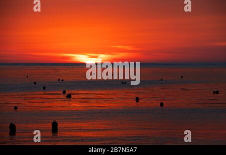 Roter Sonnenaufgang in Marsascala, Malta.St Thomas Bay, Marsaskala, Malta.Natural Sunset Sunrise over the Sea or Ocean with Boat in the Background.Dramatic Sky Stockfoto