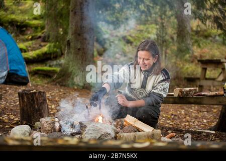 Mann und Frau, die auf dem Lagerfeuer im Wald am Ufer des Sees Kaffee zubereiten, Feuer machen und grillen. Glückliches Paar, das Finnland erkundet. Skandinavien Stockfoto