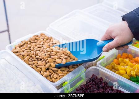 Geschälte Mandeln in der Nähe. Für Vegetarier. Nahaufnahme eines Verkäufers mit einem Spachtel, bei dem Mandeln aus einem Ladengeschäft für Trockenobst entnommen werden. Stockfoto