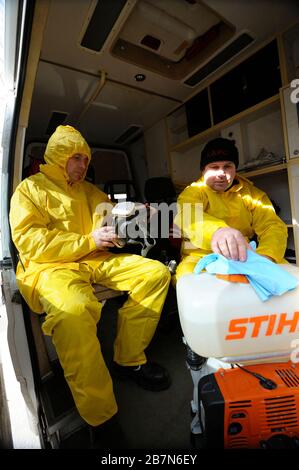 Sanitäter sitzen im Rettungswagen und tragen gelbe Schutzkleidung und Masken zur Desinfektion von Coronavirus auf. Februar 2020. Kiew, U Stockfoto