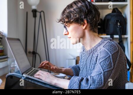 Junge Frau, die von zu Hause aus arbeitet. Kaukasische Kurzhaarangestellte mit Brille, die online von zu Hause aus auf einem Computerlaptop arbeitet Stockfoto