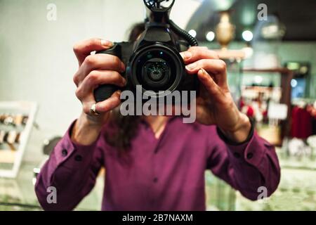 Nahaufnahme und Frontansicht im selektiven Fokus eines Mannes, der B-Roll Filmen soll, Kamera ohne Stativ frei halten kann, mit DSLR-Kamera und Objektivreflexionen. Stockfoto