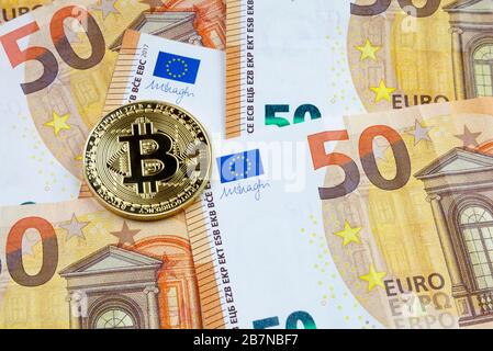 Nahaufnahme einer goldenen Bitcoin-Münze auf einem Stapel von 50 Euro-Banknoten. Stockfoto