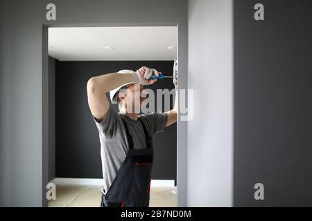 Junger lächelnder Reparaturmann in leerer Wohnung stehend und mit Schraubendreher Strom fixieren Stockfoto