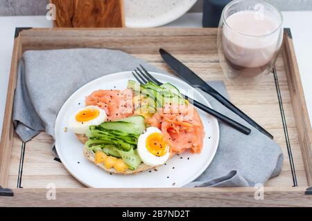 Sandwich mit Toastbrot, Räucherlachs, Frischkäse, geschnittener Gurke und gekochten Eiern auf weißem Teller. Stockfoto