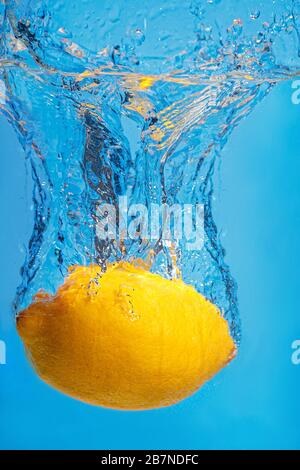 Frische Zitrone fällt mit einem Spritzer auf blauem Grund in Wasser