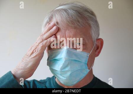 Beim tragen einer Gesichtsmaske hält der ältere Mann eine Hand an der Stirn Stockfoto