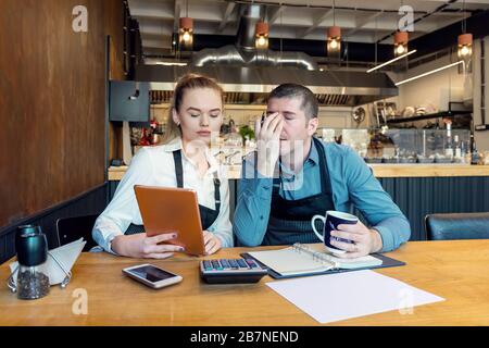 Besorgte Unternehmer berechnen die Finanzen - kleine Restaurantunternehmer KMU gehen wegen Coronavirus Pandemie bankrott - junge Frau und Mann mit h Stockfoto