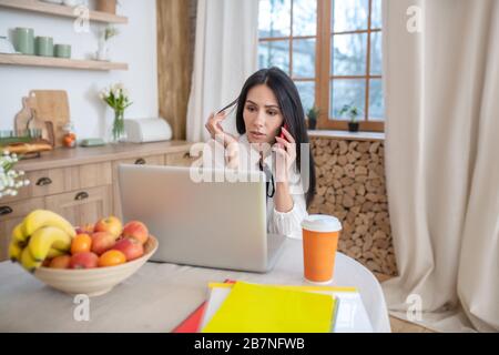Junge Frau überprüft Laptop und hält Haarsträhne Stockfoto
