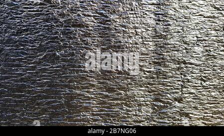 Silberfarbene, raue, zerknitterte Folientextur. Zerknitterte glänzende Metallfolientextur oder Hintergrund für das Design. Dünnes Blatt mit silberfarbenem Blatthintergrund mit glänzendem Stockfoto