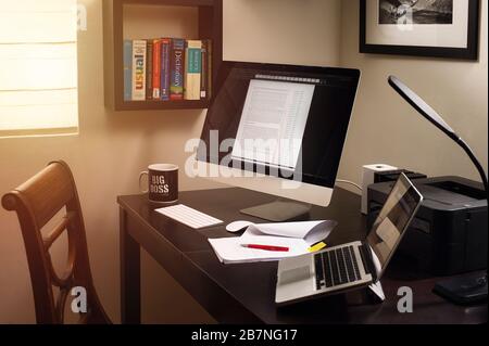 Arbeiten Sie von zu Hause aus mit zwei Computerbildschirmen in warmer Atmosphäre mit Kaffee Stockfoto