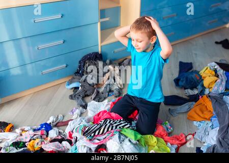 Der kleine Junge verzweifelte mit dem Chaos in seiner Kleidung in seinem Schlafzimmer. Stockfoto