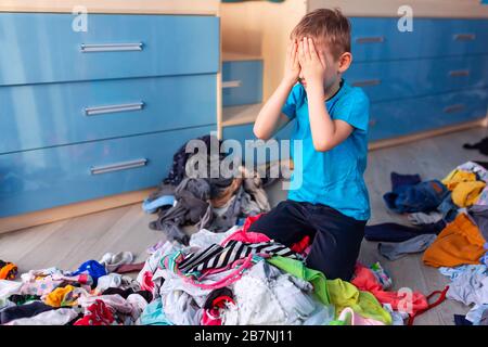 Der kleine Junge verzweifelte mit dem Chaos in seiner Kleidung in seinem Schlafzimmer. Stockfoto