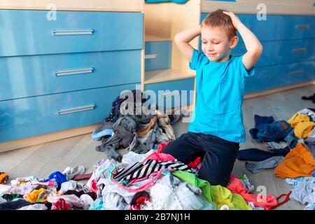 Der kleine Junge verzweifelte mit dem Chaos in seiner Kleidung in seinem Schlafzimmer. Stockfoto