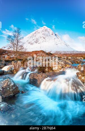 Kaskadierende Wasserfälle in Glen Etive mit einem verschneiten Buachaille Etive Mor Berg im Hintergrund in Glencoe in den schottischen Highlands Stockfoto