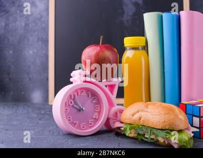 Schulessen, Bücher, Saft, rosafarbener Wecker, Schultafel für den Text mit Kreide. Schulpause. Freier Speicherplatz für Text. Kopierbereich Stockfoto