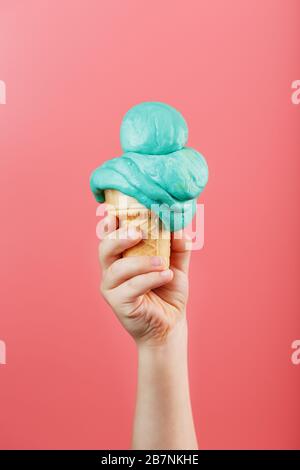 Eis in der Hand eines Kindes schmilzt auf einem rosafarbenen Hintergrund. Der Waffelkegel mit blauem Eis schmilzt. Stockfoto
