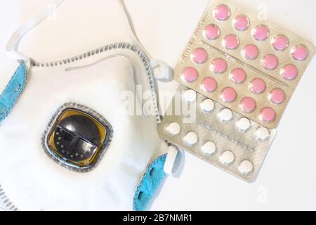 Atemschutzmaske auf weißem Hintergrund mit Tabletten oder Pillen Draufsicht. Medizinische Maske flach gelegt Stockfoto