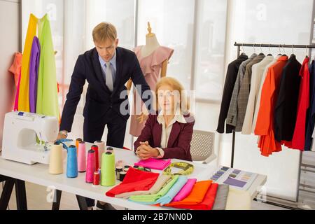 Professionelle Designer, junge Männer und ältere Frauen im Arbeitsraum mit verschiedenen Stofffarbschemata Stockfoto