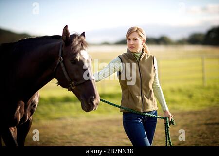 Porträt eines jungen Erwachsenen stehendes Mädchen mit einem Pferd in einem Feld. Stockfoto