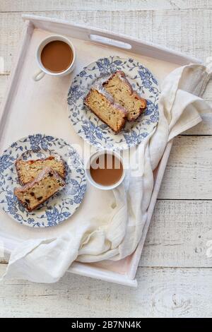 Hausgebackener Bananenkuchen mit Schokoladentropfen und zwei Kaffeetassen auf einem weißen Tablett Stockfoto