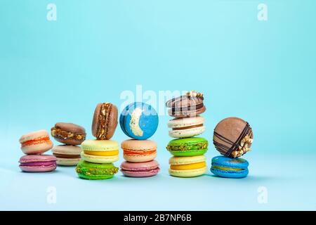 Verschiedene Arten von farbenfrohen süßen französischen Kakenmakaron oder Makronen in Stapeln auf blauem Hintergrund, verschiedene bunte Mandelplätzchen, Pastell und helles c Stockfoto