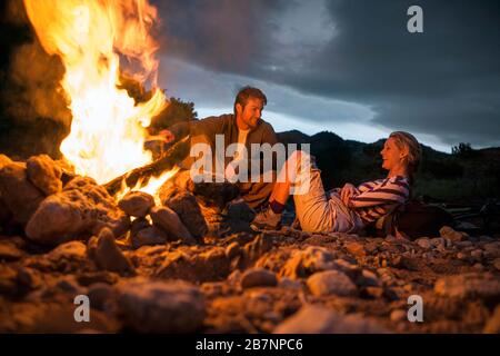 Junges Paar erholt sich und lacht am glühenden Lagerfeuer. Stockfoto