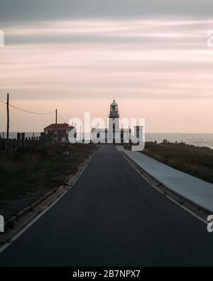 Schöner Leuchtturm am Ende der langen Straße bei Sonnenuntergang in Galicien, Spanien Stockfoto