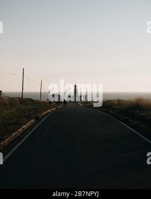 Schöner Leuchtturm am Ende der langen Straße bei Sonnenuntergang in Galicien, Spanien Stockfoto