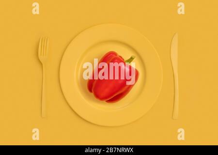 Rote Paprika oben auf gelber Platte, Messer und Gabel. Auf gelbem Hintergrund. Die Ansicht von oben. Stockfoto